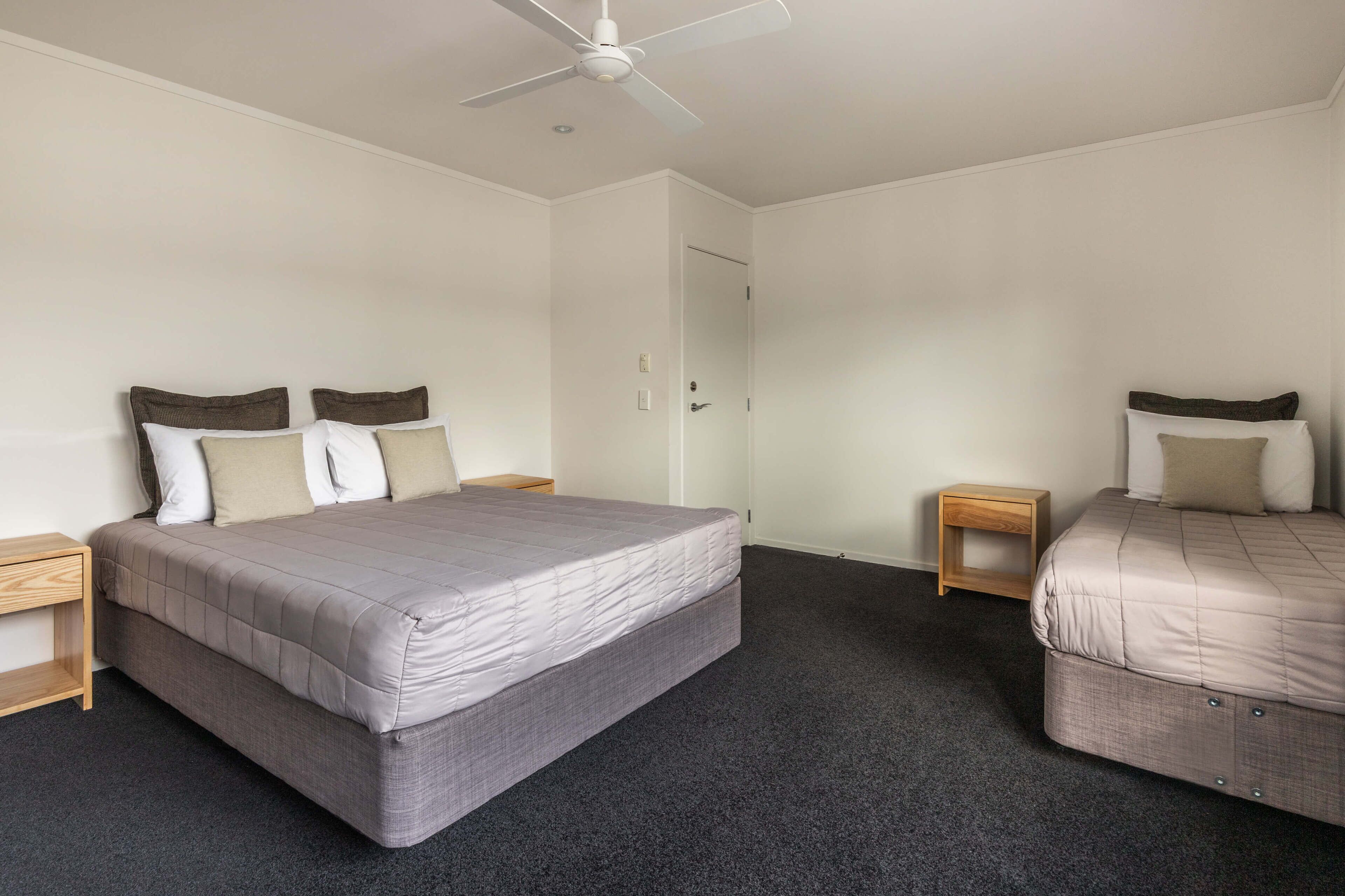 A bedroom with a large bed, a smaller bed, a ceiling fan, and a door.