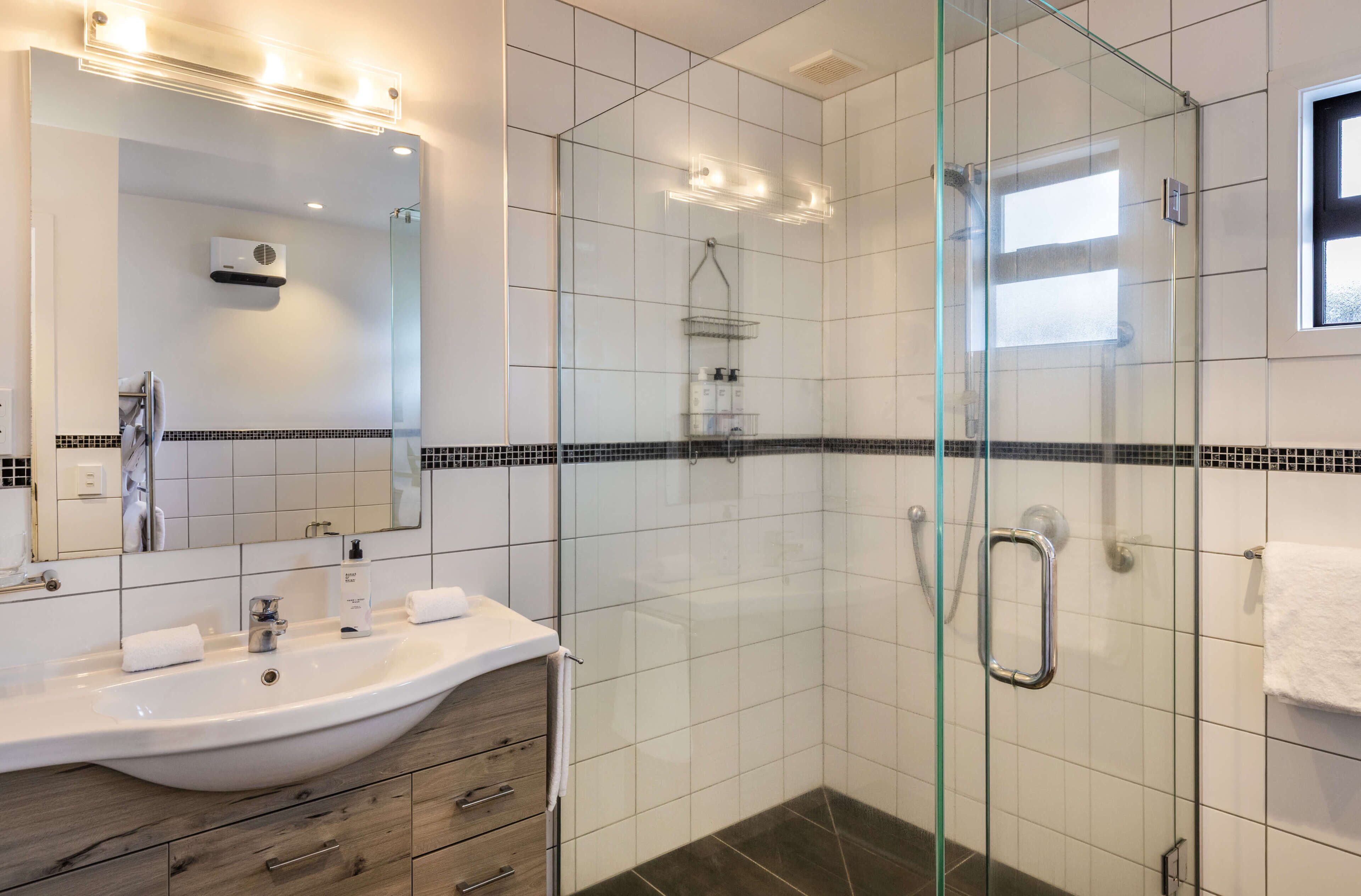 A modern bathroom with a glass-enclosed shower, a large mirror, and a vanity with a sink and towel rack.