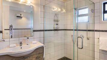 A modern bathroom with a glass-enclosed shower, a large mirror, and a vanity with a sink and towel rack.