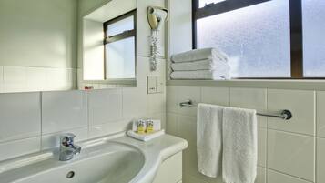 A bathroom with a white sink, a mirror, a window, and two towels hanging on a rack.