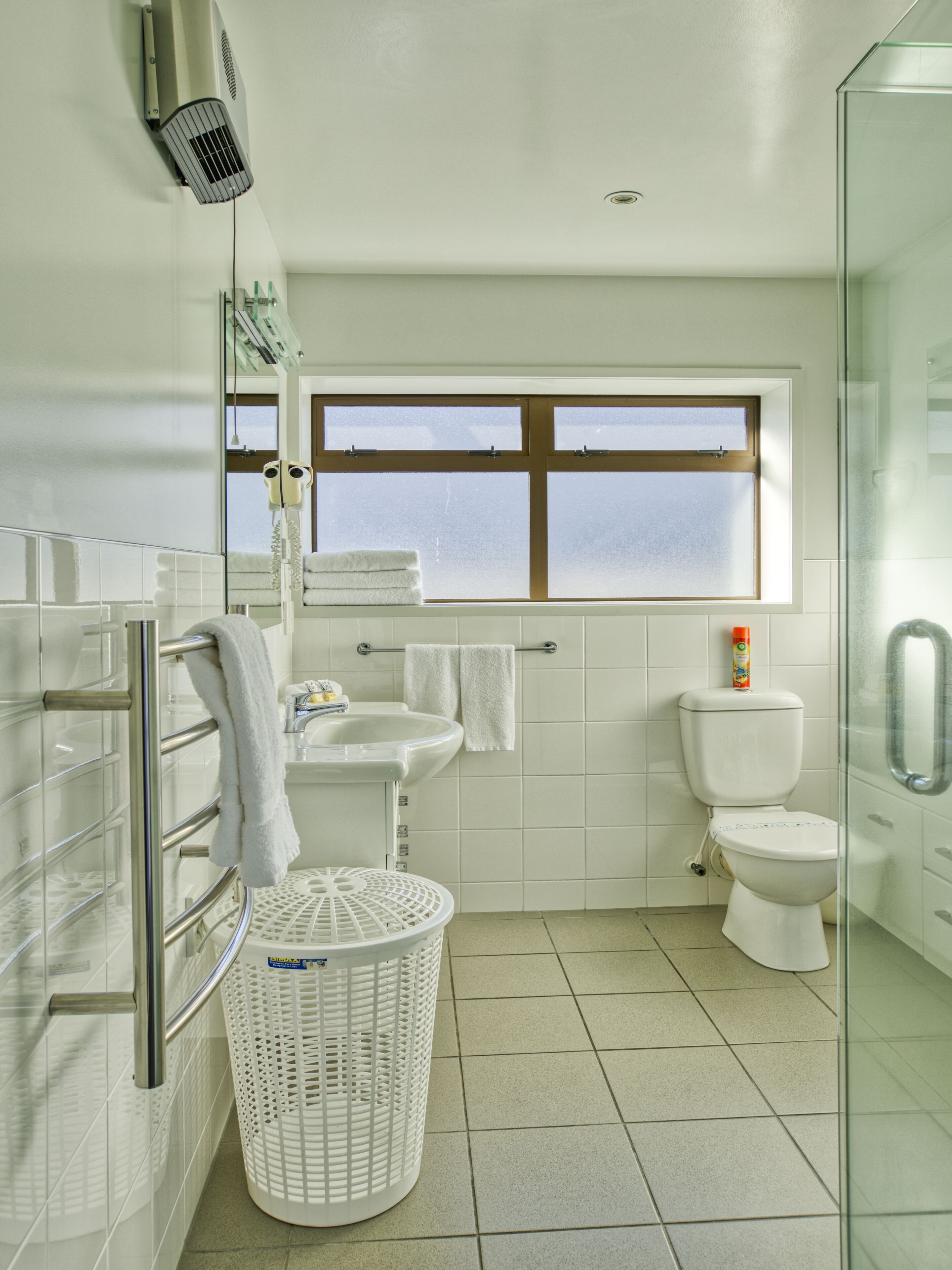 A modern bathroom with a glass shower enclosure, a toilet, a sink, and a window.