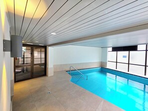 Une piscine intérieure à l’eau d’un bleu cristallin, dotée d’un sol carrelé et d’un plafond au design moderne.
