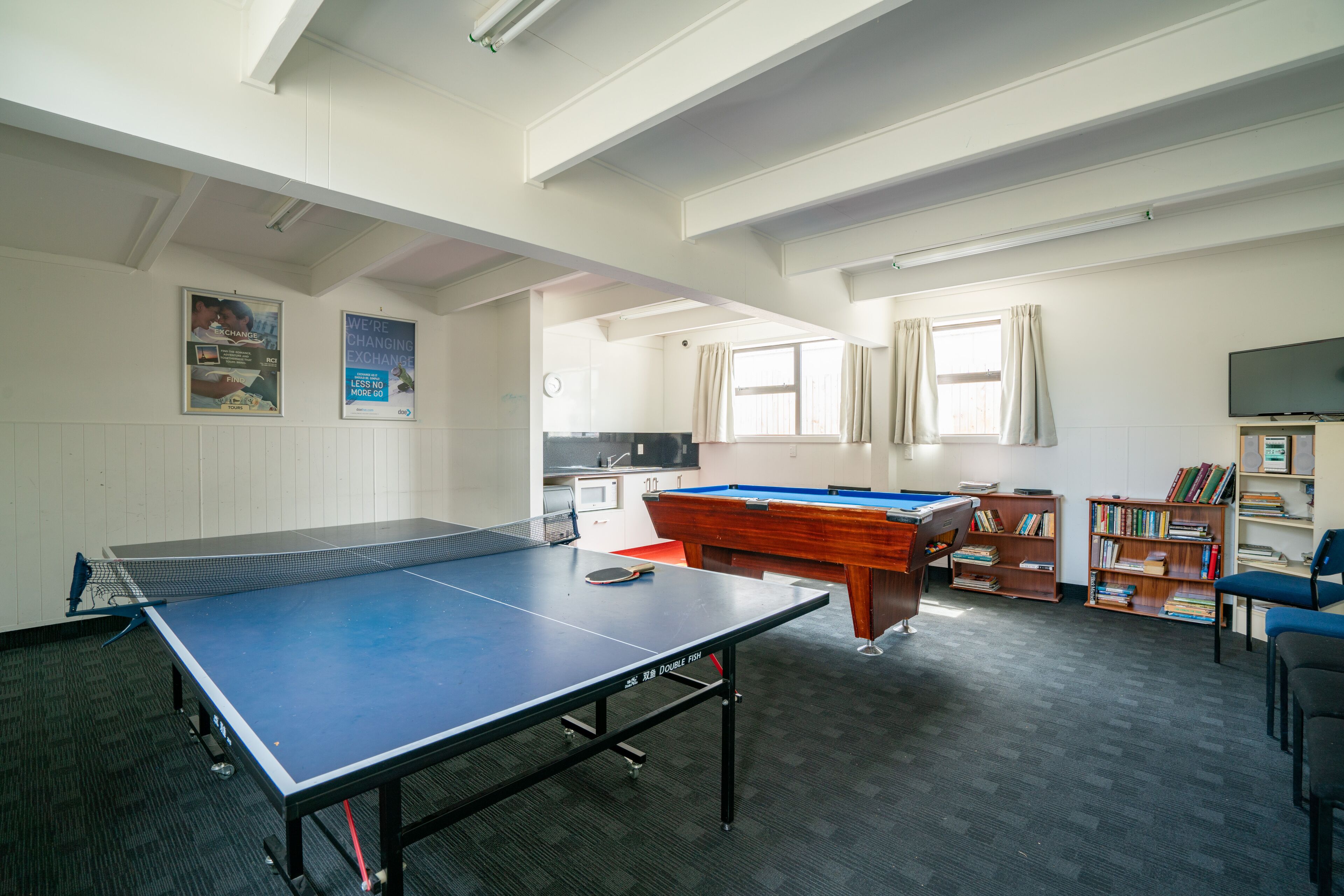 A room with a ping pong table, a pool table, and a bookshelf.