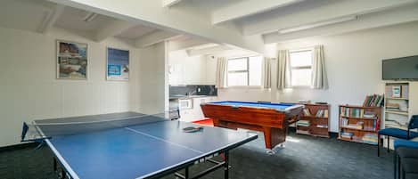 Una habitación con mesa de ping pong, mesa de billar y una estantería.