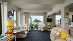 Une chambre d’hôtel avec vue sur la mer, un canapé, des fauteuils, une petite table avec une lampe et un téléviseur.
