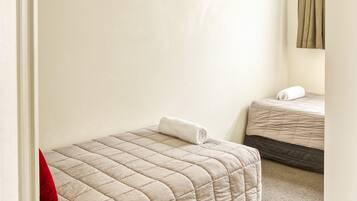 A bedroom with two beds, a wooden nightstand, a red pillow, and a ceiling light.