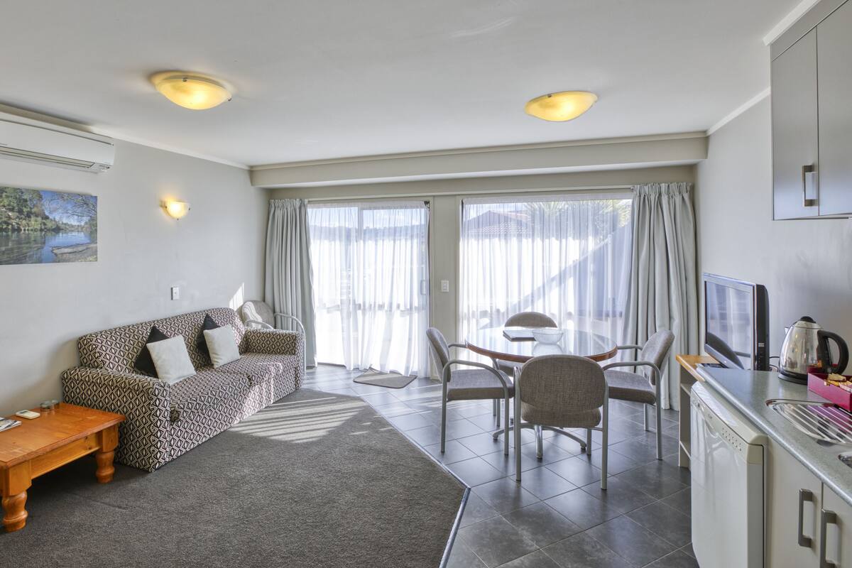 Ein modernes Wohnzimmer mit einer Couch, einem Esstisch mit Stühlen und einer Küchenzeile inklusive Herd und Fernseher.