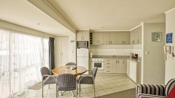 A modern kitchen with white cabinets, a microwave, and a stove. There is a dining area with a round table and patterned chairs.