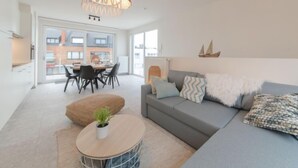 Una sala de estar moderna con un sofá gris, una mesa redonda de madera y una lámpara colgante.