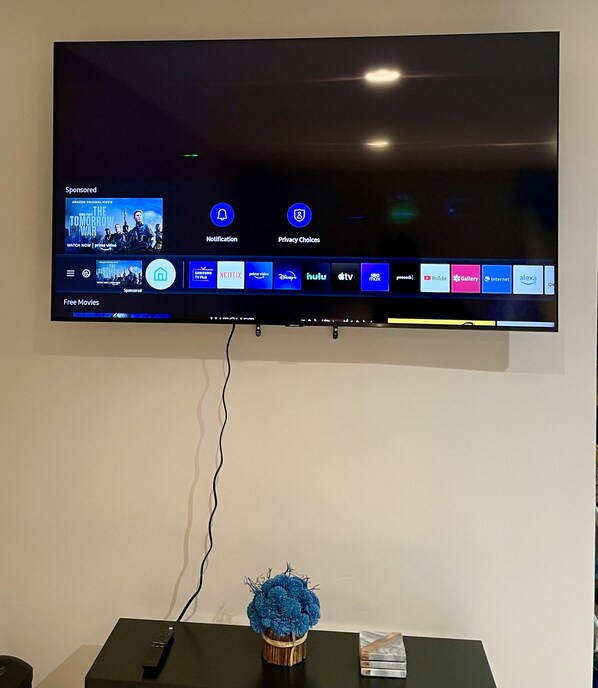 A flat-screen TV mounted on a wall with a remote control on a stand below it.