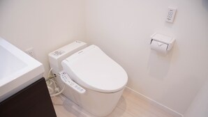 A modern bathroom with a toilet, a bidet, and a paper towel dispenser. - Basic Stay Sugamo (北区)