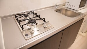 A kitchen with a gas stove, a microwave, and a stainless steel sink. - Basic Stay Sugamo (北区)