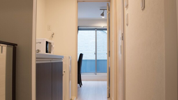 A narrow hallway with a kitchen area on the left, a view of the sea through a glass door at the end, and a door on the right. - Basic Stay Sugamo (北区)