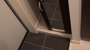 A narrow hallway with a dark-colored door and a white wall. - Basic Stay Sugamo (北区)