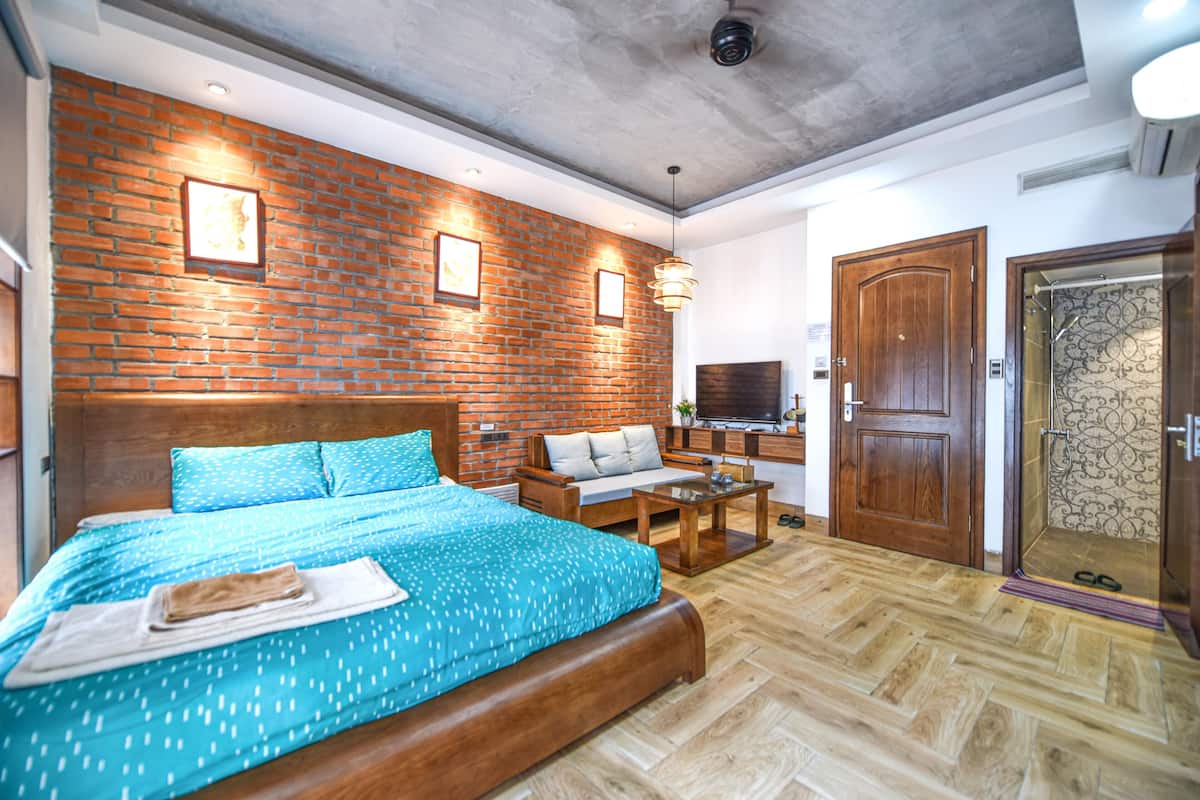 A bedroom with a brick wall, wooden bed, and a TV.