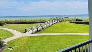 Un balcone con vista sull'oceano e una zona verde con una passerella in legno.