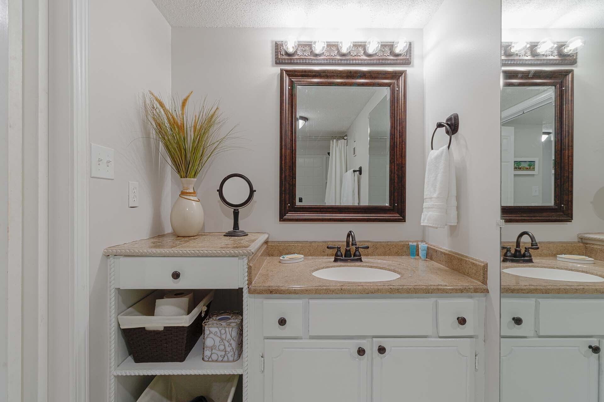 A bathroom with a vanity, two sinks, a mirror, a towel rack, and a plant.