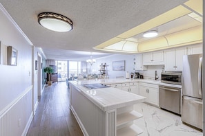 Cocina amplia con muebles blancos, una isla grande y electrodomésticos de acero inoxidable.