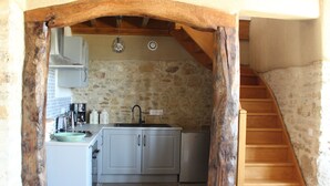 Una cocina con paredes de piedra, una escalera de madera y una viga rústica en el techo.