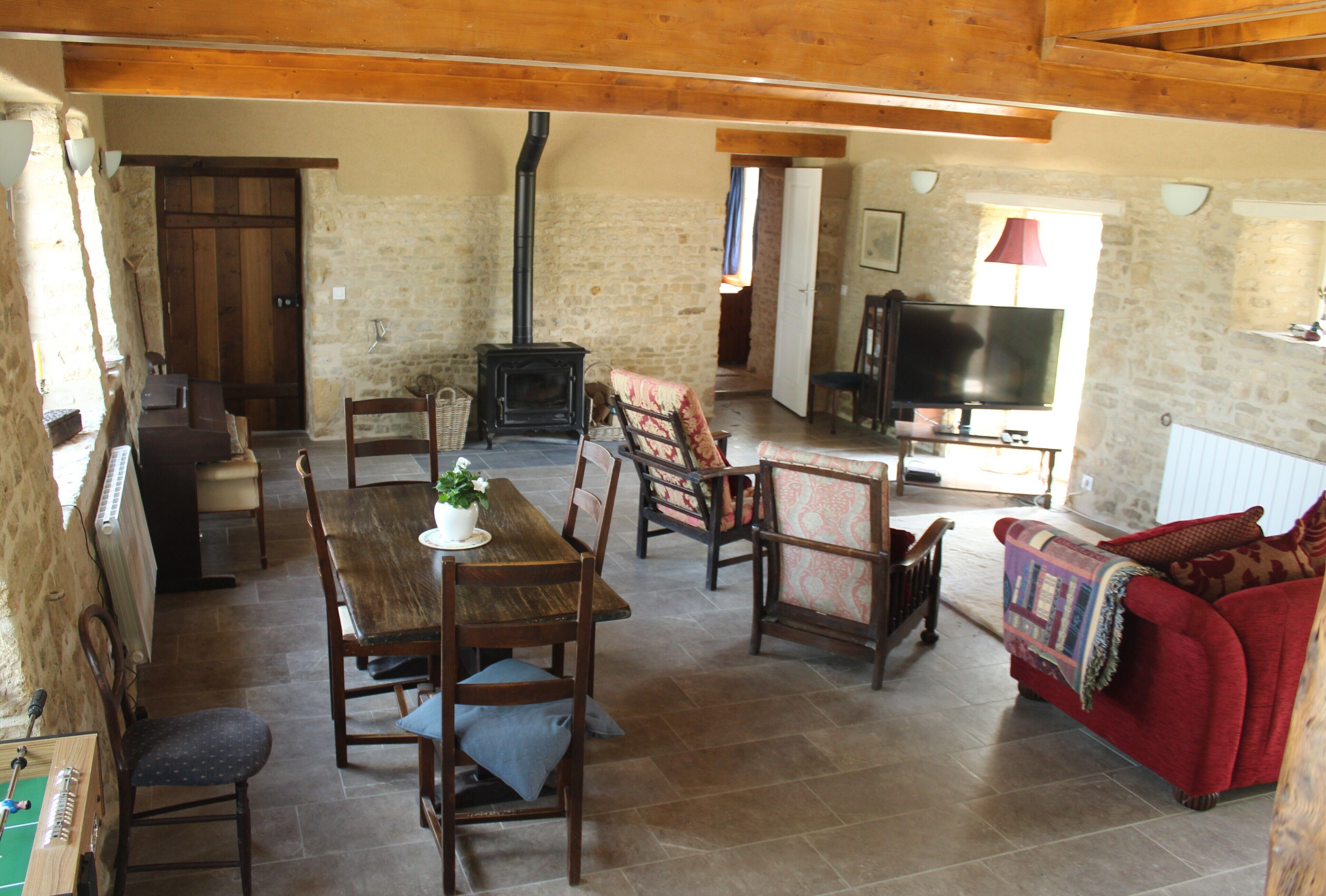 A rustic living room with a wooden table, chairs, a red sofa, a television, and a fireplace.