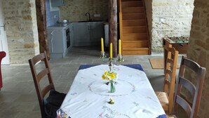 Un comedor con una mesa preparada para dos personas, un jarrón con flores y una escalera que lleva a una cocina.