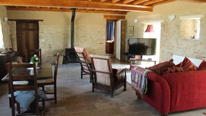 Una sala de estar rústica con paredes de piedra, vigas de madera, chimenea, televisor y un sofá rojo.