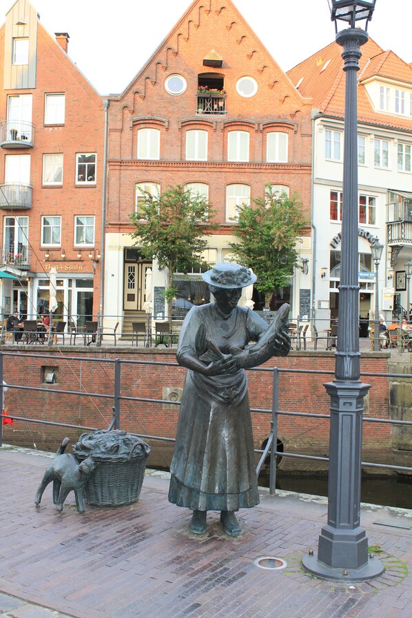 A statue of a woman reading a book, a lamp post, and a brick building with a balcony in the background.