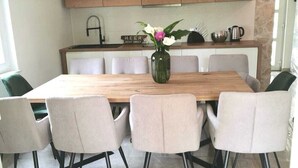 Un coin repas avec une table en bois et six chaises, un vase rempli de fleurs et, en arrière-plan, un mur en pierre.
