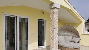 Un espace extérieur abrité, doté d’un pilier en pierre, d’une entrée avec porte vitrée et d’un canapé en osier.