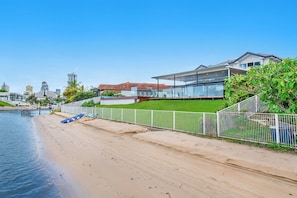 A beachfront property with a modern house, a fenced garden, and a boat on the sand.