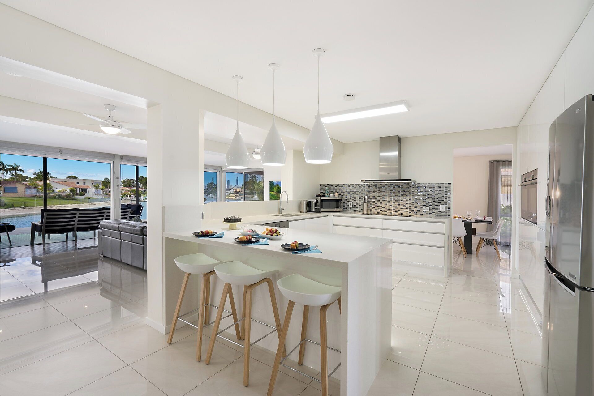 A modern kitchen with a central island, bar stools, a dining area with a view, and a large refrigerator.