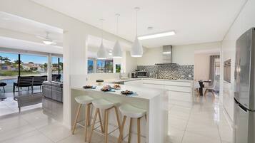 A modern kitchen with a central island, bar stools, a dining area with a view, and a large refrigerator.
