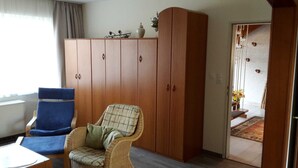 Une pièce comprenant une chaise en osier, un fauteuil bleu et une armoire en bois.