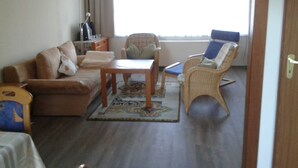 Un salon avec un canapé, une petite table, un fauteuil en osier et une fenêtre avec des rideaux.