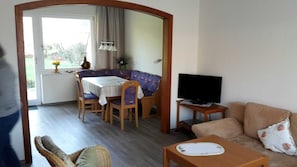 Uma sala de estar com sofá, televisão, mesa de jantar com cadeiras e janela com cortinas.
