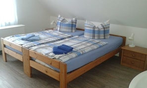 Uma cama de madeira com colcha xadrez azul e branca, dois travesseiros e duas toalhas azuis dobradas.