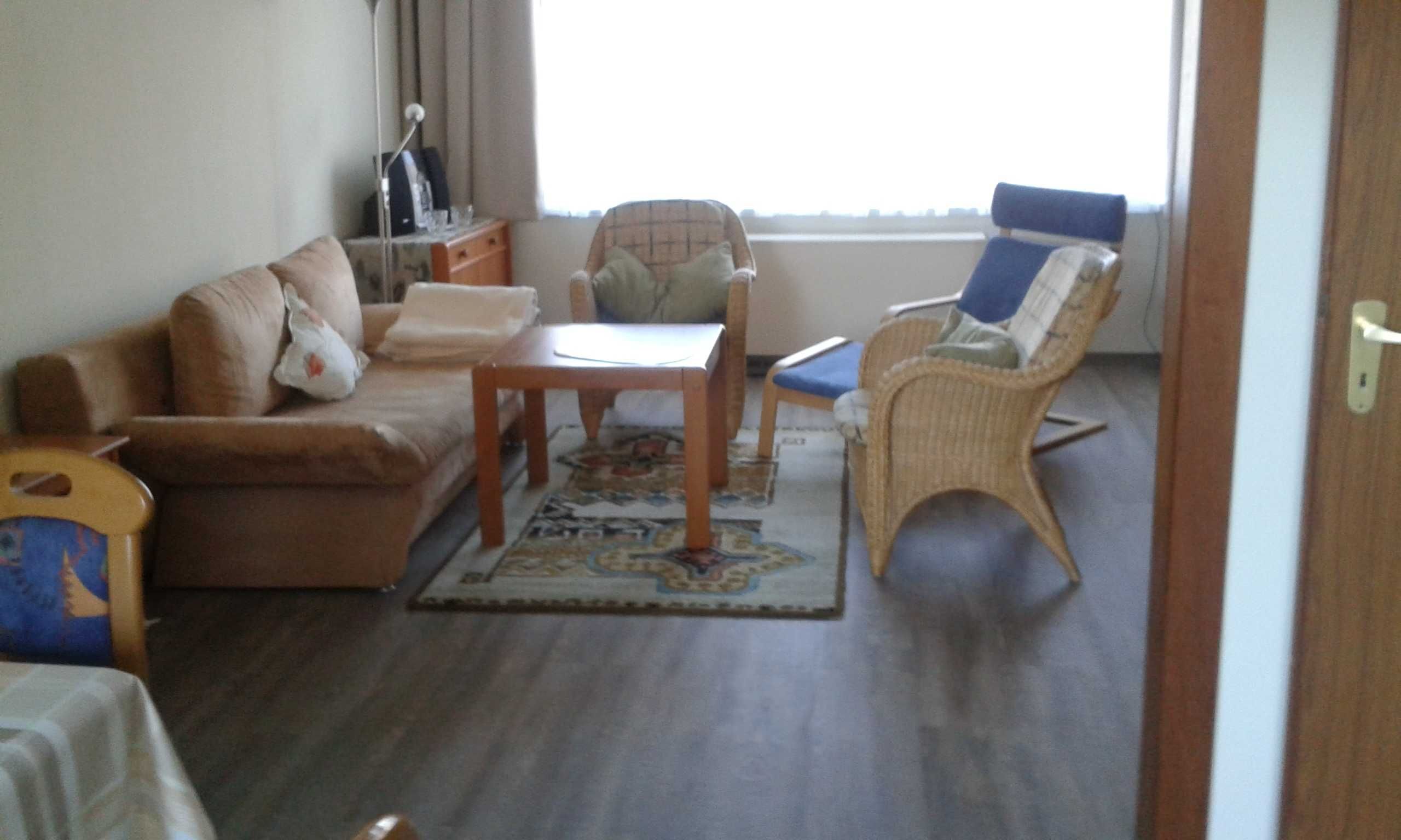 A living room with a sofa, a small table, a wicker chair, and a window with curtains.