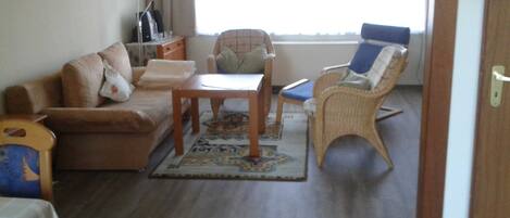 A living room with a sofa, a small table, a wicker chair, and a window with curtains.