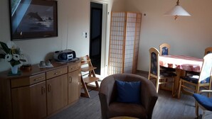 A room with a wooden cabinet, a chair with a blue cushion, a table with a red tablecloth, and a traditional Japanese sliding door. - Eg+og - Ferienhaus Topmann (Büsum)