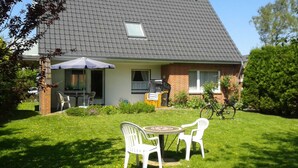A house with a tiled roof, a covered patio with outdoor furniture, and a lawn with a table and chairs. - Eg+og - Ferienhaus Topmann (Büsum)