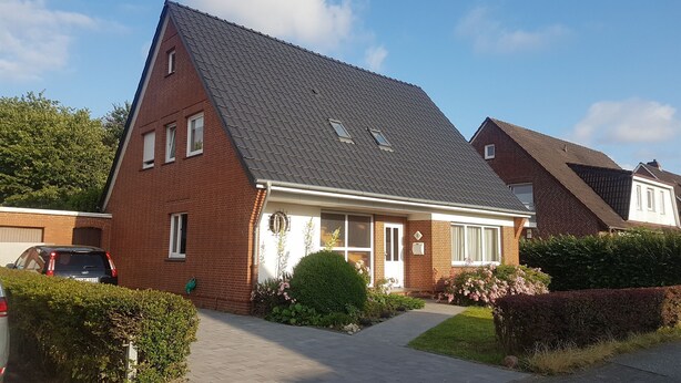 A two-story house with a sloped roof, a front porch, and a small garden. - Eg+og - Ferienhaus Topmann (Büsum)