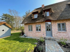 Ein traditionelles Backsteinhaus mit Strohdach, einem kleinen angebauten Schuppen und einem gepflasterten Zufahrtsweg.