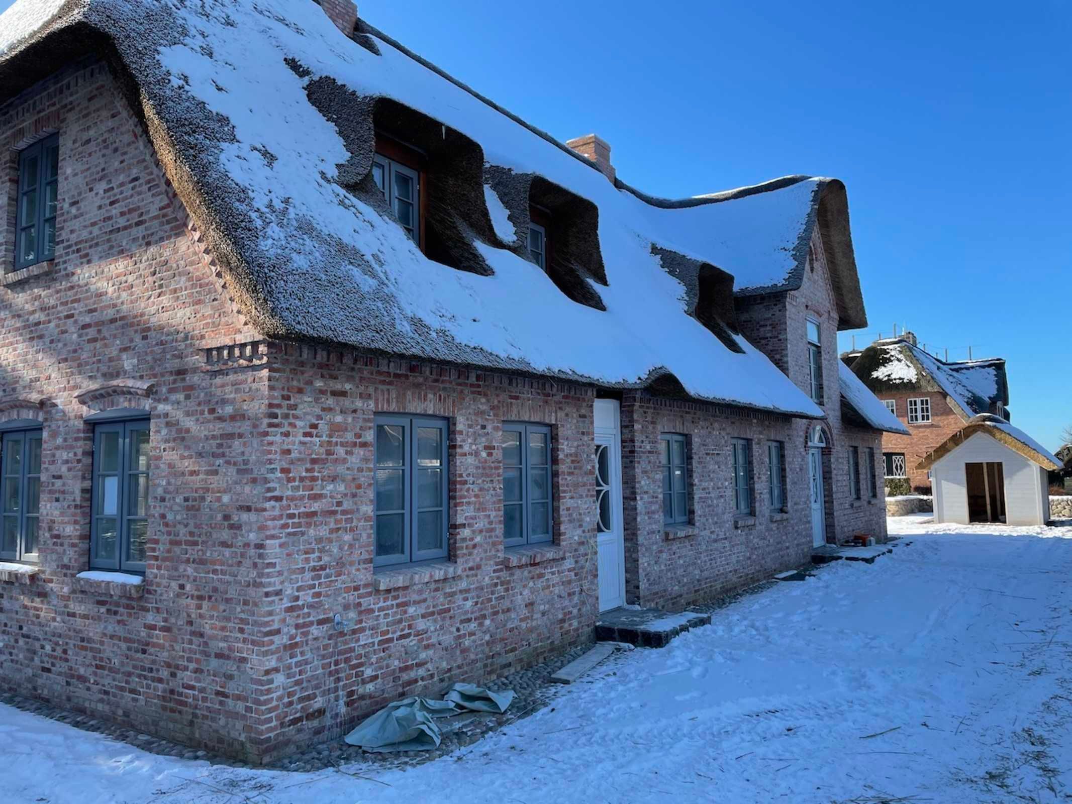 Un edificio de ladrillo con un techo inclinado cubierto de nieve, varias ventanas y una chimenea visible.