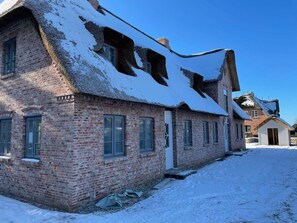 A brick building with a steeply pitched roof covered in snow, multiple windows, and a visible chimney.