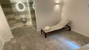 Una sala de spa amb un llit de massatge, un petit rentapeus i una dutxera de vidre.