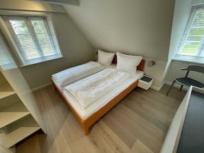 A bedroom with a bed, a nightstand, a chair, and a window with blinds.
