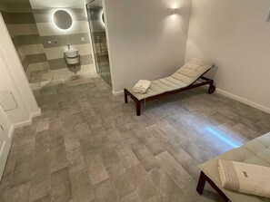 A spa room with a massage table, a small sink, and a glass shower enclosure.