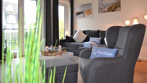 A modern living room with a grey sofa, a coffee table, and a view of the outdoors. - App. Ankerplatz mit 2 SZ und 2 Balkonen - Appartement mit 2 SZ (Kellenhusen (Ostsee))