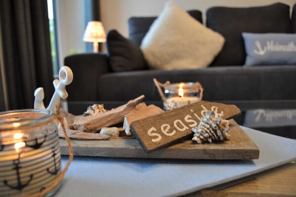 A cozy living room with a wooden board displaying the word "Seasons," a glass candle holder, and a small figurine.