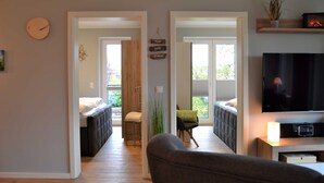 A modern living room with a sofa, a TV, and a bookshelf. There is a staircase leading to a balcony with a view of trees. - App. Ankerplatz mit 2 SZ und 2 Balkonen - Appartement mit 2 SZ (Kellenhusen (Ostsee))